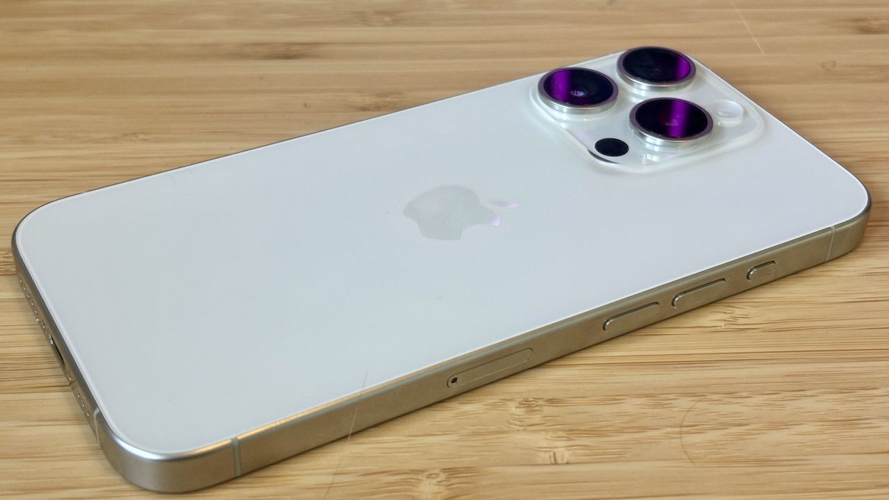 A grey titanium iPhone 15 Pro camera phone on a wooden desk