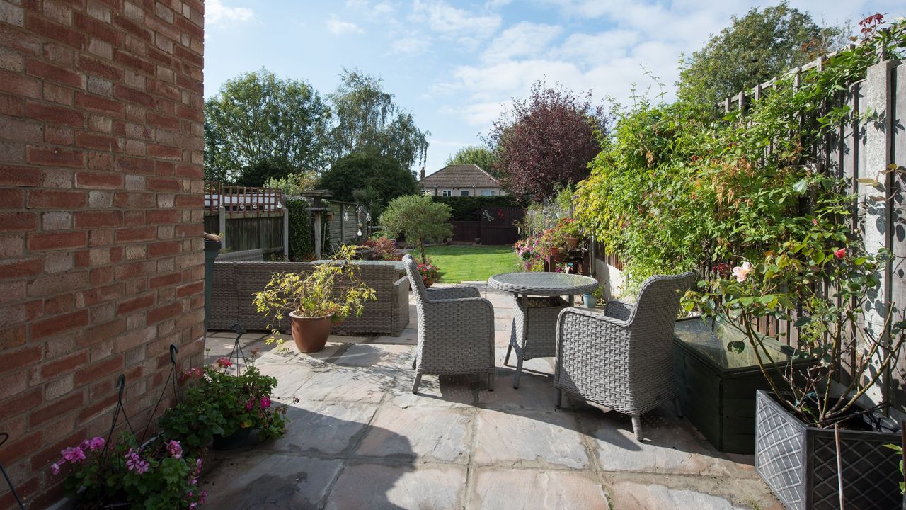 A general view of a grey rattan garden table and chairs for two on a patio surrounded by a high garden fence