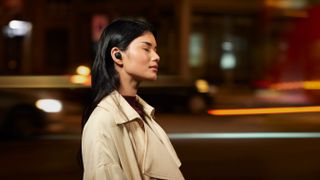 Sony WF-1000XM5 A woman wearing the Sony WF-1000XM4 true wireless earbuds with her eyes closed and in the background there's a blurry cityscape