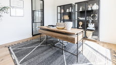 Large modern home office featuring a dark beige central desk with drawers on gray area rug, glass front cabinet with minimal against the wall