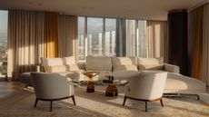 beige living room in high-rise apartment with cream and yellow curtains, large L-shaped beige sofa, two beige armchairs, a beige patterned rug, two yellow glass coffee tables, and a dark timber-wrapped column