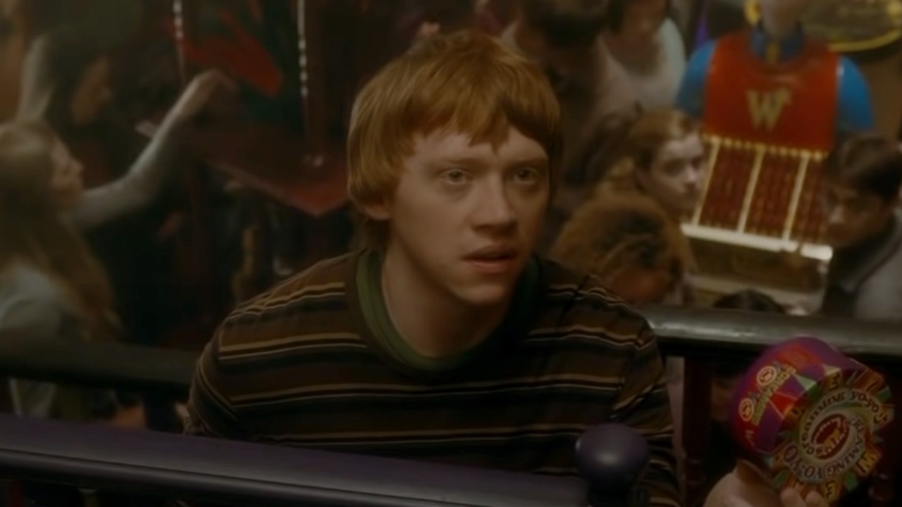 Rupert Grint as Ron Weasley holding a box of candy and scowling in Harry Potter and the Half-Blood Prince, the brother of Charlie Weasley.