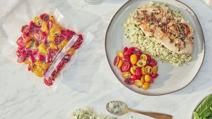 A food vacuum seal bag with tomatoes inside beside a plate with the same tomatoes, a pan-friend chicken breast, and rice.