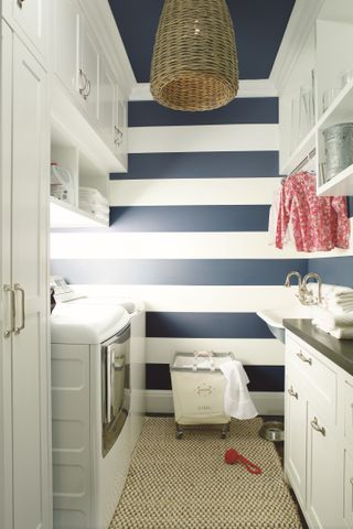 A small utility room with blue and white striped wallpaper and white cabinets on either side