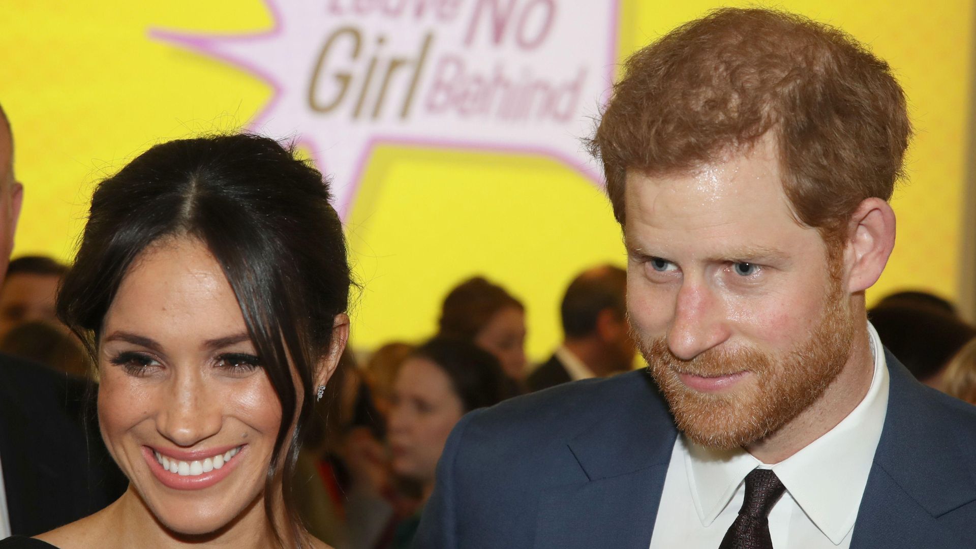 Meghan Sussex and Prince Harry in front of a yellow sign