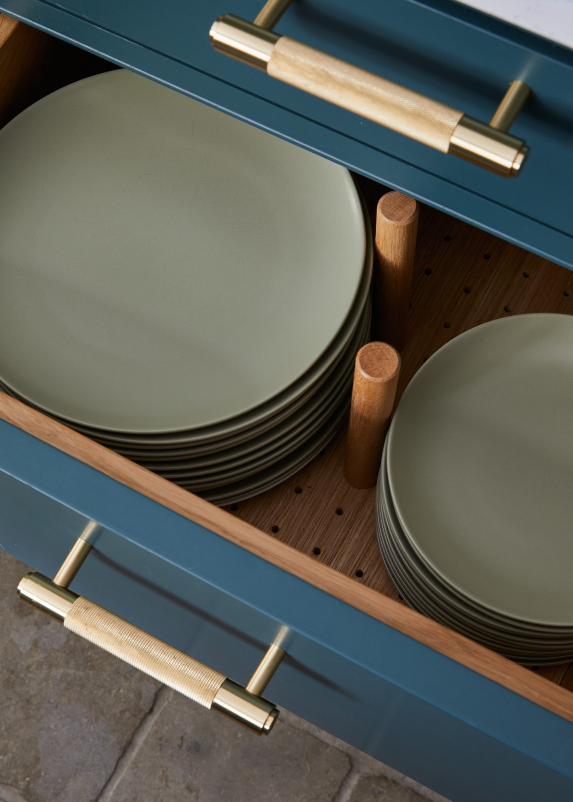 Stacks of sage green plates in a deep kitchen drawer, separated with wooden pegs to keep them in place and prevent them touching the other piles