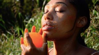 A close-up of a face with eyes closed, holding an orange ball.