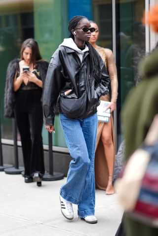 woman wearing leather jacket, hoodie, jeans and adidas sambas