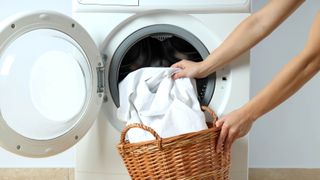 Bedsheets being loaded into a washing machine from a hamper