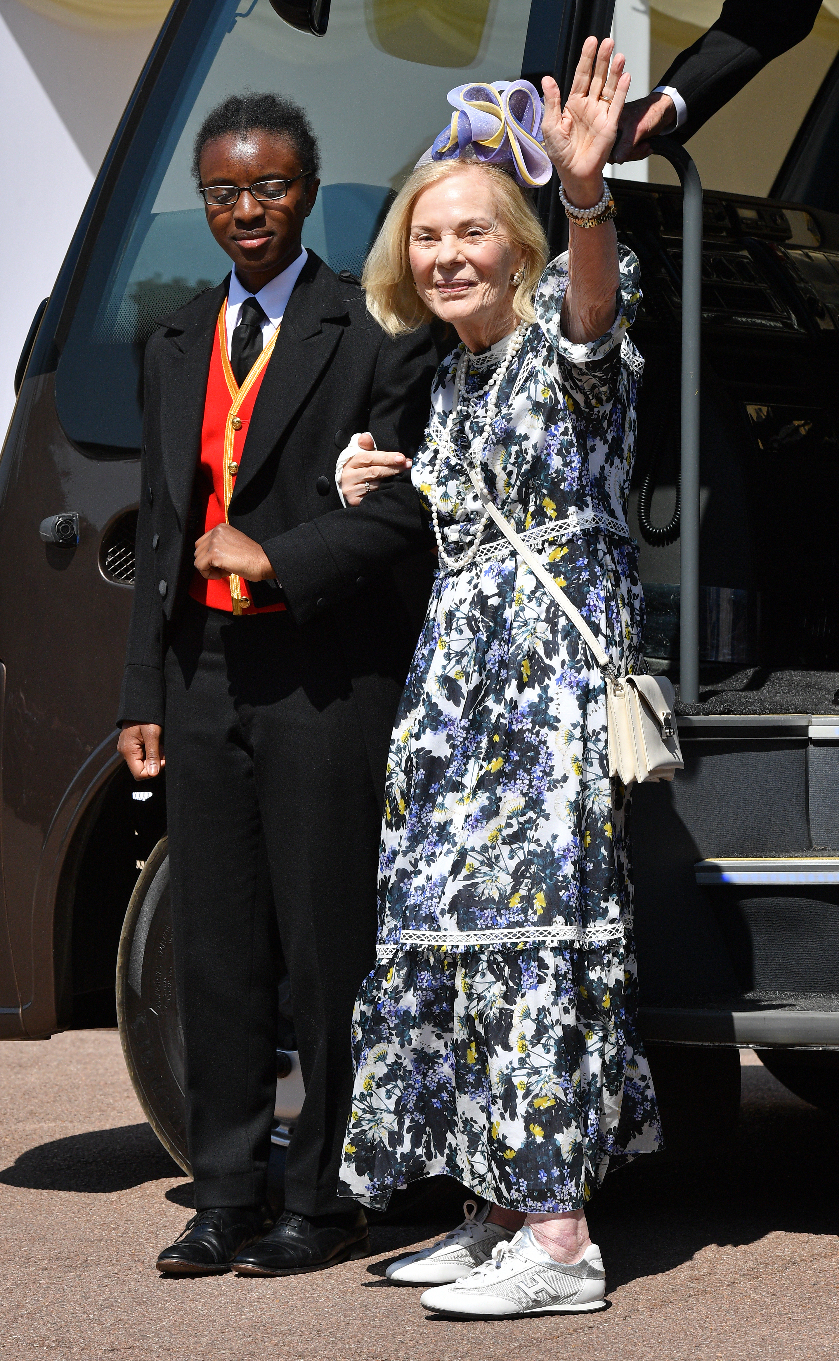 The Duchess of Kent wearing a floral dress waving on the arm of a palace employee