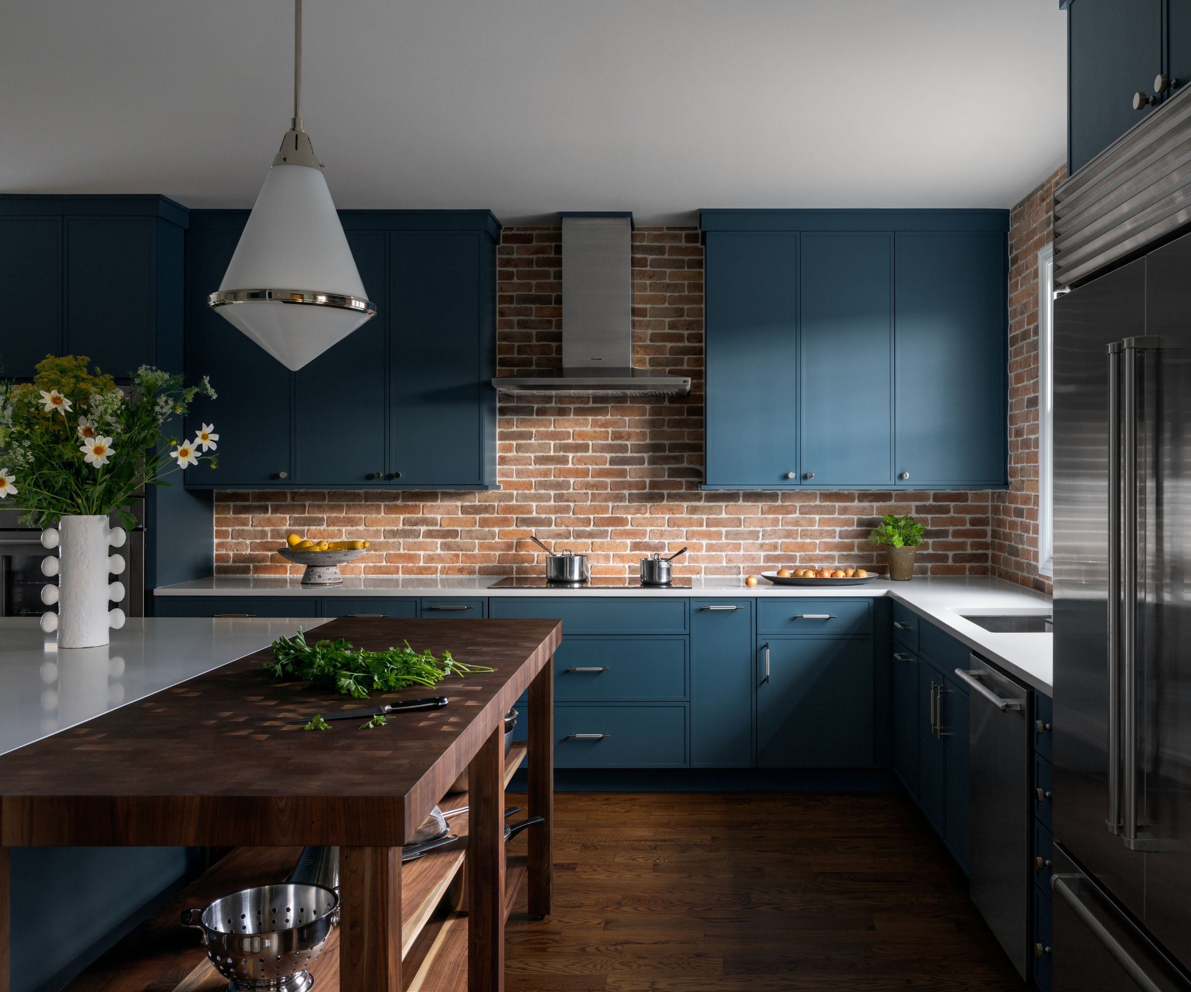 Kitchen with blue cabinetry, a brick backsplash and a wooden butchers block attached to a white marble topped island