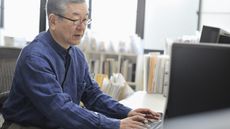 An older man works on his computer at his desk in the office.