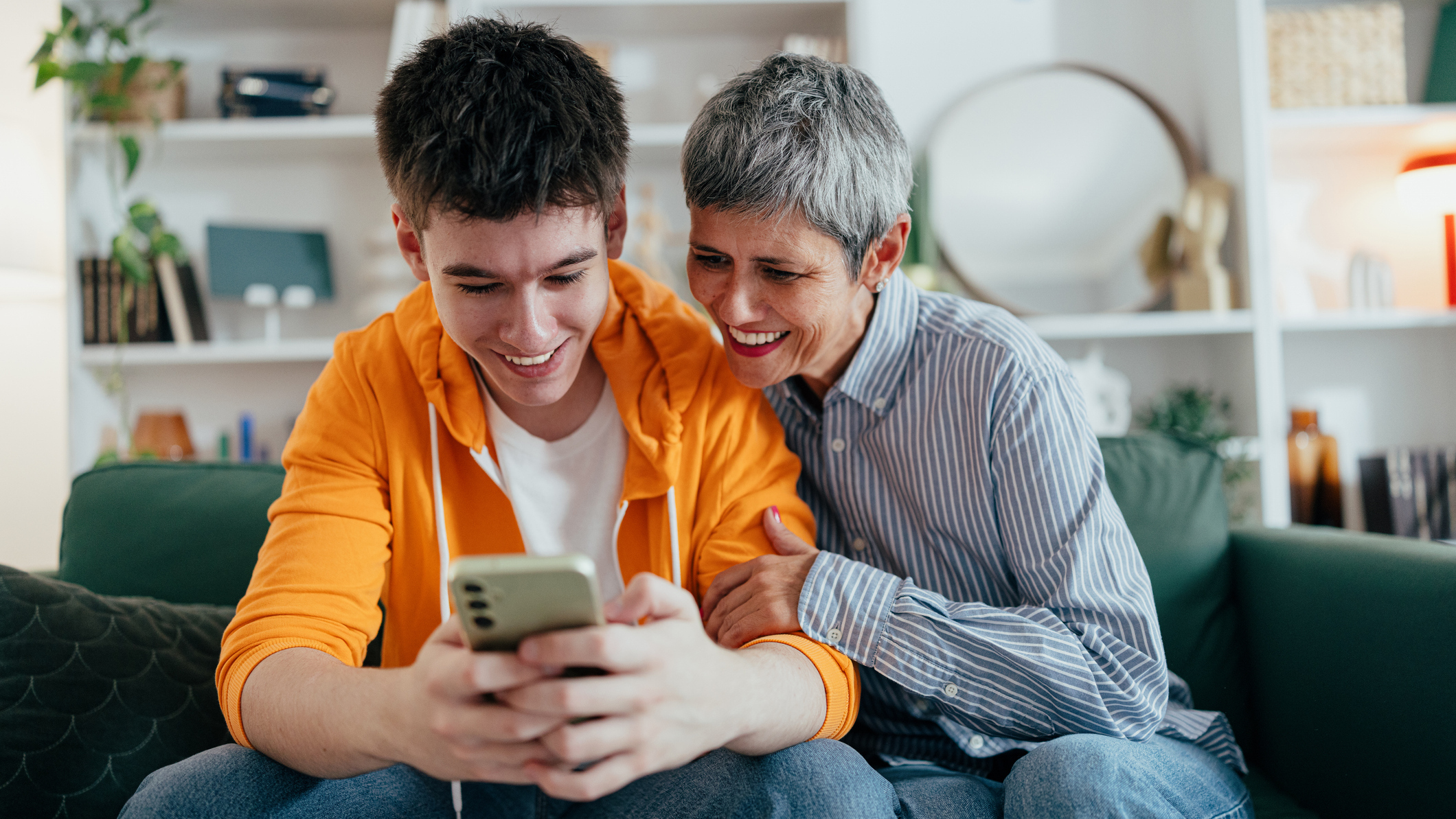 Parent and teen smiling, both looking at a phone