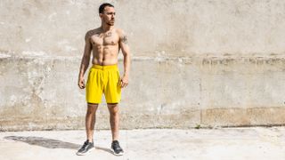 Man outside doing a standing abs workout with shirt off in yellow shorts
