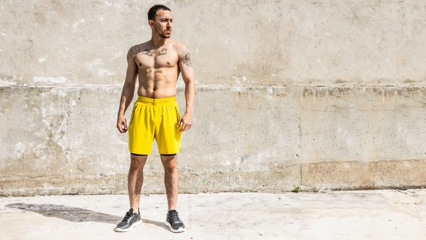 Man outside doing a standing abs workout with shirt off in yellow shorts