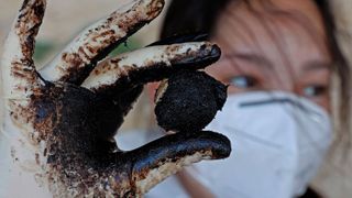 An Israeli soldier displays a tar ball during cleanup operation at the Sharon Beach National Park, north of Tel Aviv city, on Feb. 22