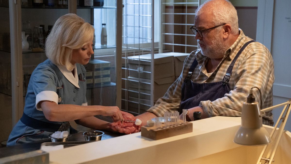 Helen George in a nurse&#039;s uniform as Trixie puts cotton wool on a cut on Cliff Parisi&#039;s hand as Fred in Call the Midwife. 