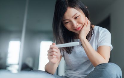 A woman smiling because she is happy with her pregnancy test result after following guidance on how to increase fertility