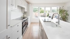 Interior view of a domestic dove grey kitchen, with painted white walls, island with quartz worktop, chrome tap, grey crushed velvet bar stools, stainless steel range cooker oven, chrome tap and skylight - for article on kitchen cleaning mistakes