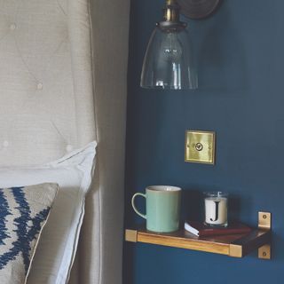 A bedroom with blue-painted walls and a bedside shelf in place of a bedside table