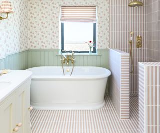 bathroom with white freestanding bath, shower area defined by half height walls, pink and white striped bathroom tiling