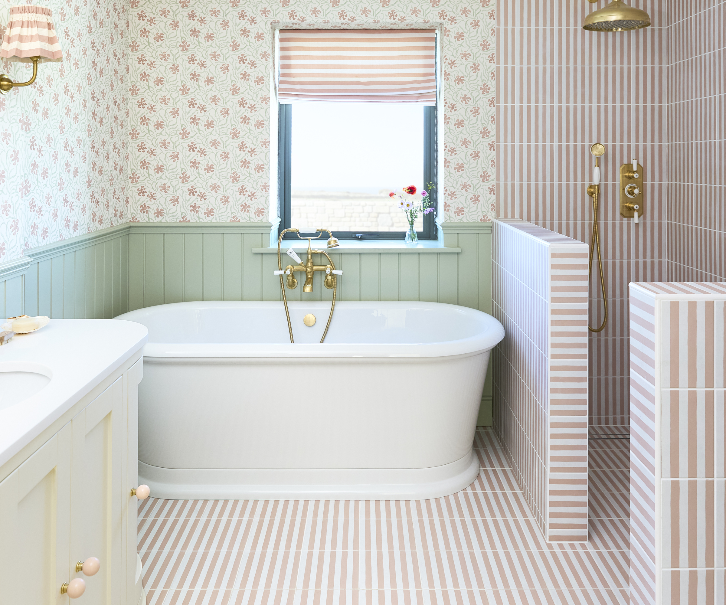 bathroom with white freestanding bath, shower area defined by half height walls, pink and white striped bathroom tiling