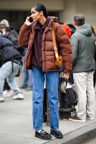 woman wearing puffer jacket, hoodie, jeans, and loafers