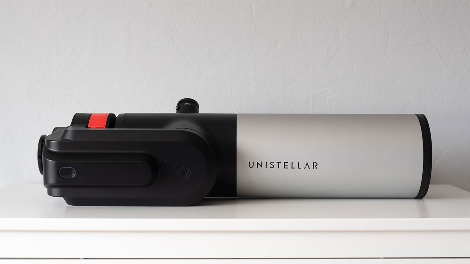 Unistellar eVscope 2 laying down on a white surface with a white wall as the background