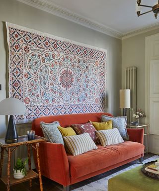 soft blue painted living room with a velvet orange couch and a large wall hanging suzani