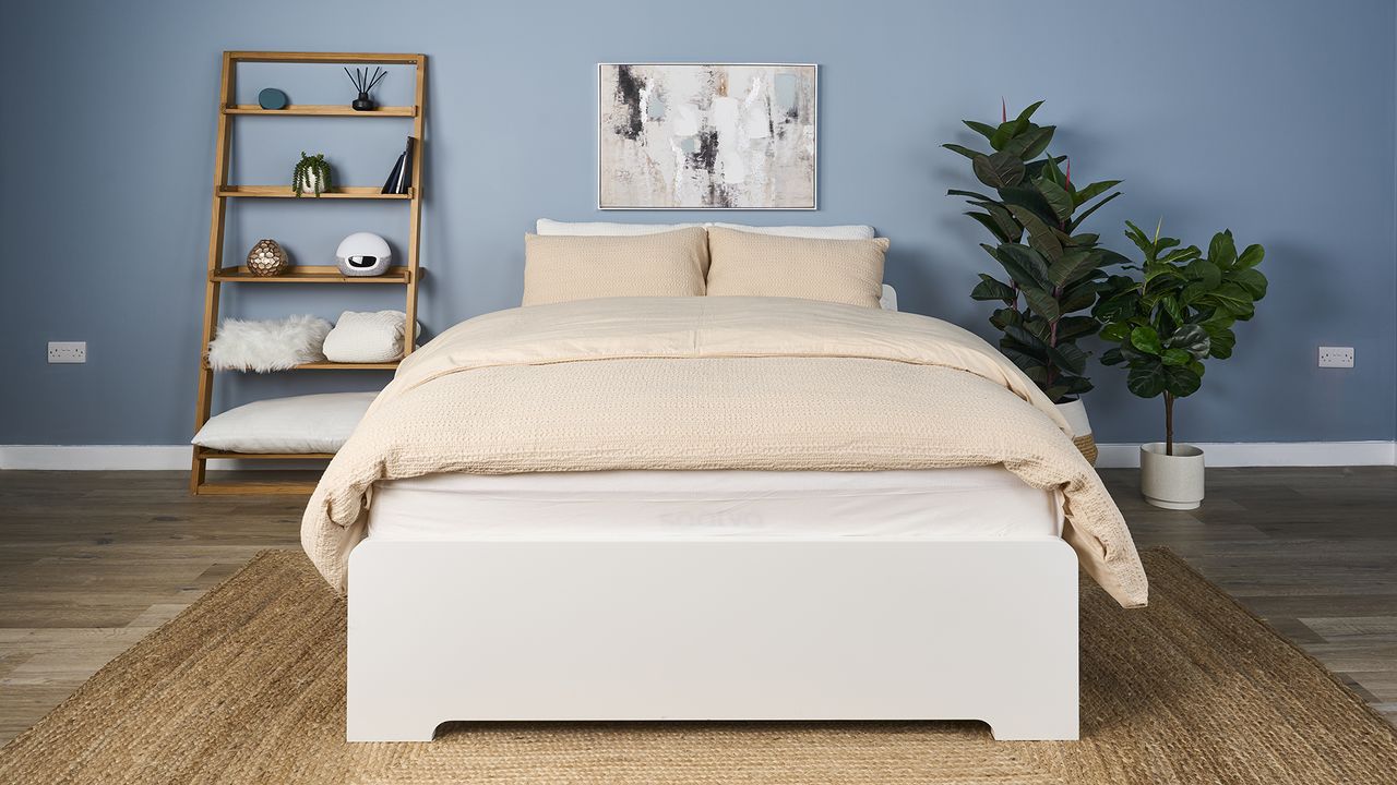 The Saatva Classic mattress dressed in a luxurious beige comforter with matching hotel style pillows and placed on a white bed frame in our Sleep Lab during the testing process