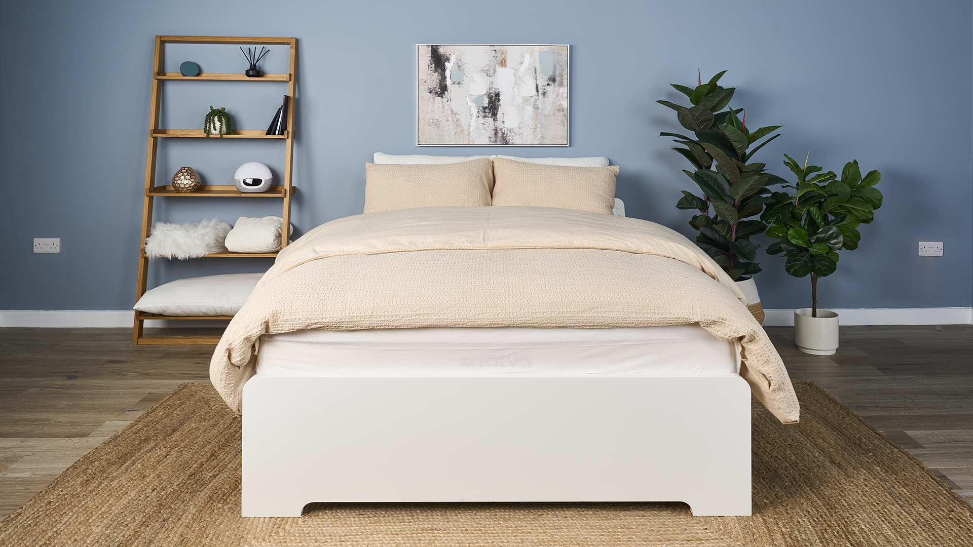 The Saatva Classic mattress dressed in a luxurious beige comforter with matching hotel style pillows and placed on a white bed frame in our Sleep Lab during the testing process