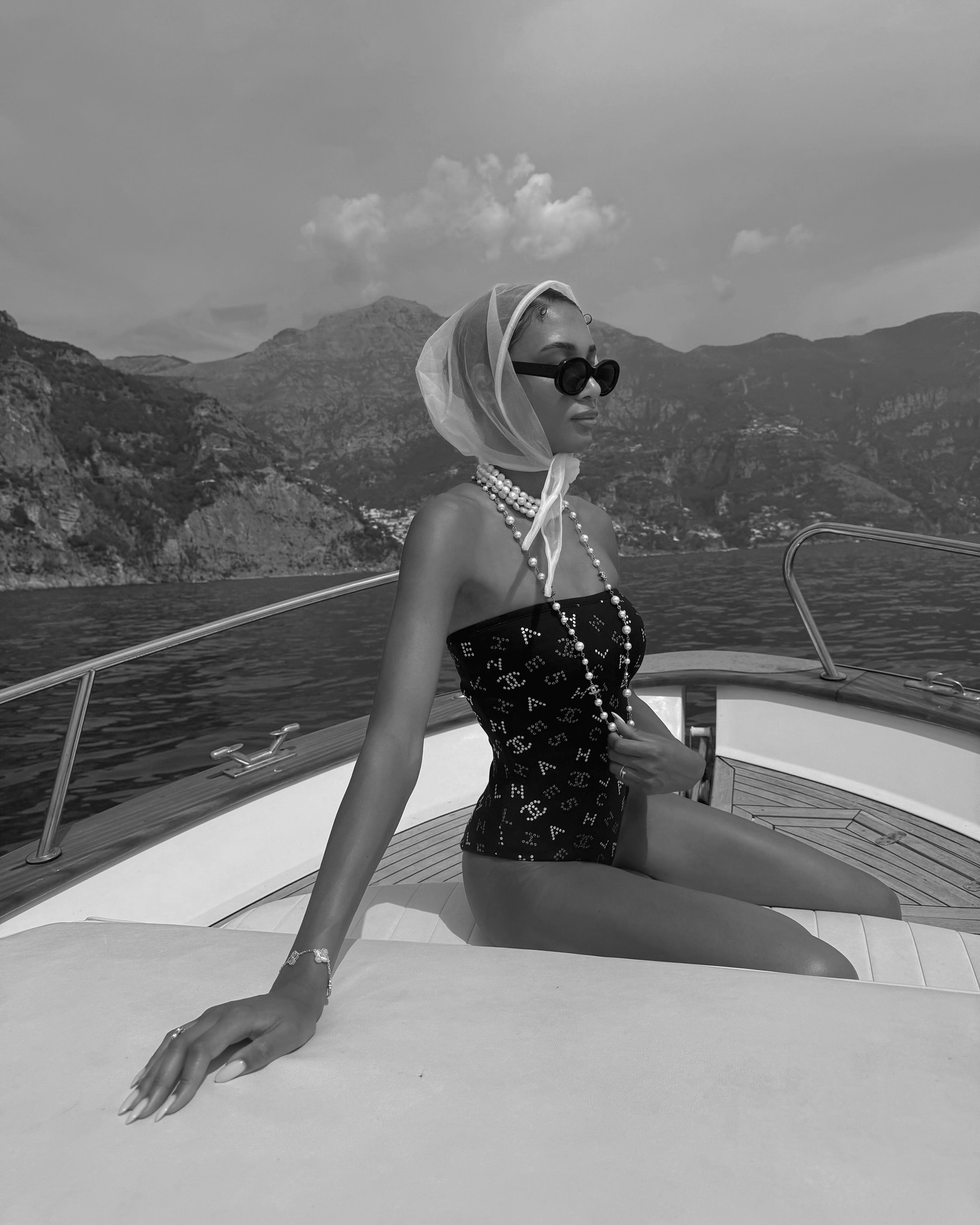 Dana Emmanuelle-Jean Ozime combines Chanel swimsuit with strands of pearls and hair scarf