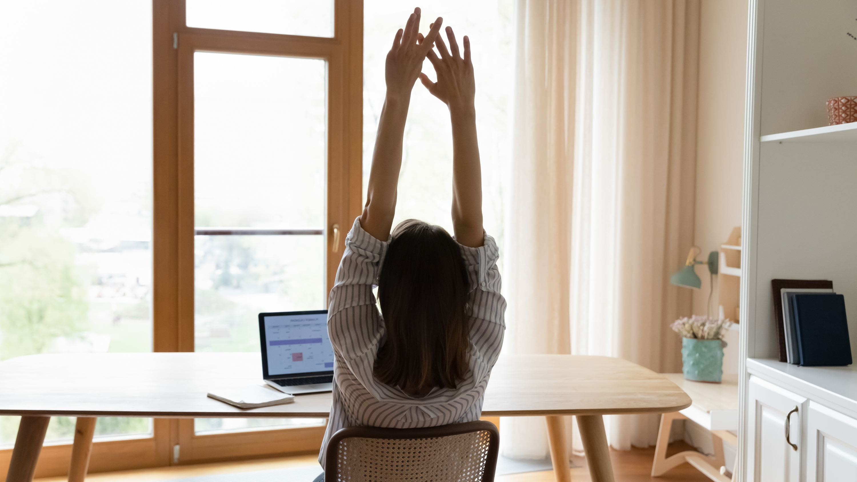 the back of a woman sat at a desk stretching her arms above her head