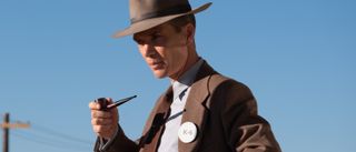 Cillian Murphy stands against a blue sky, holding a pipe, in Oppenheimer.