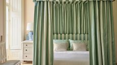 Cream bedroom with four-poster frame and striped green and cream curtains, and matching headboard