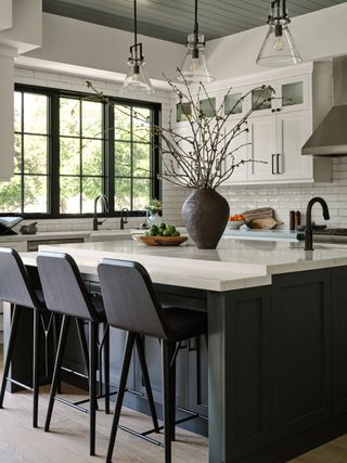 kitchen with dark gray island and cabinets and white worktops with white walls and white wall cabinets and conical clear glass pendant lights