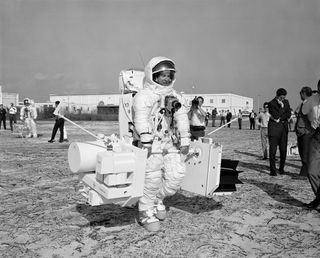 At NASA's Kennedy Space Center in Florida, Apollo 13 astronaut Jim Lovell participates in a simulation of the extravehicular activity, or "moonwalk" timeline. Lovell moves carrying two sub-package mockups of the Apollo Lunar Surface Experiments Package. In the background to the left is Apollo 13 astronaut Fred Haise.