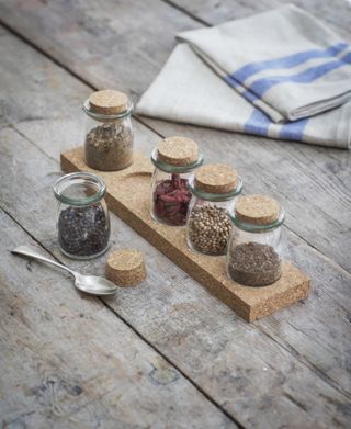 cork spice rack with four mini spice jars on wooden table, napkins