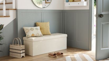 Neutral front entrance with sage green paneled walls, a cream ottoman with two pillows on top and a chevron hallway runner