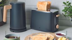 Kitchen countertop with matt grey Aldi kettle with wooden handle and matching toaster beside a wooden plate with toast to show the new Aldi kitchen appliances in stores