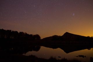 A evening shot across the lake at Cawfields with the silhouette and reflection of Cawfields crag. The sky is filled with stars