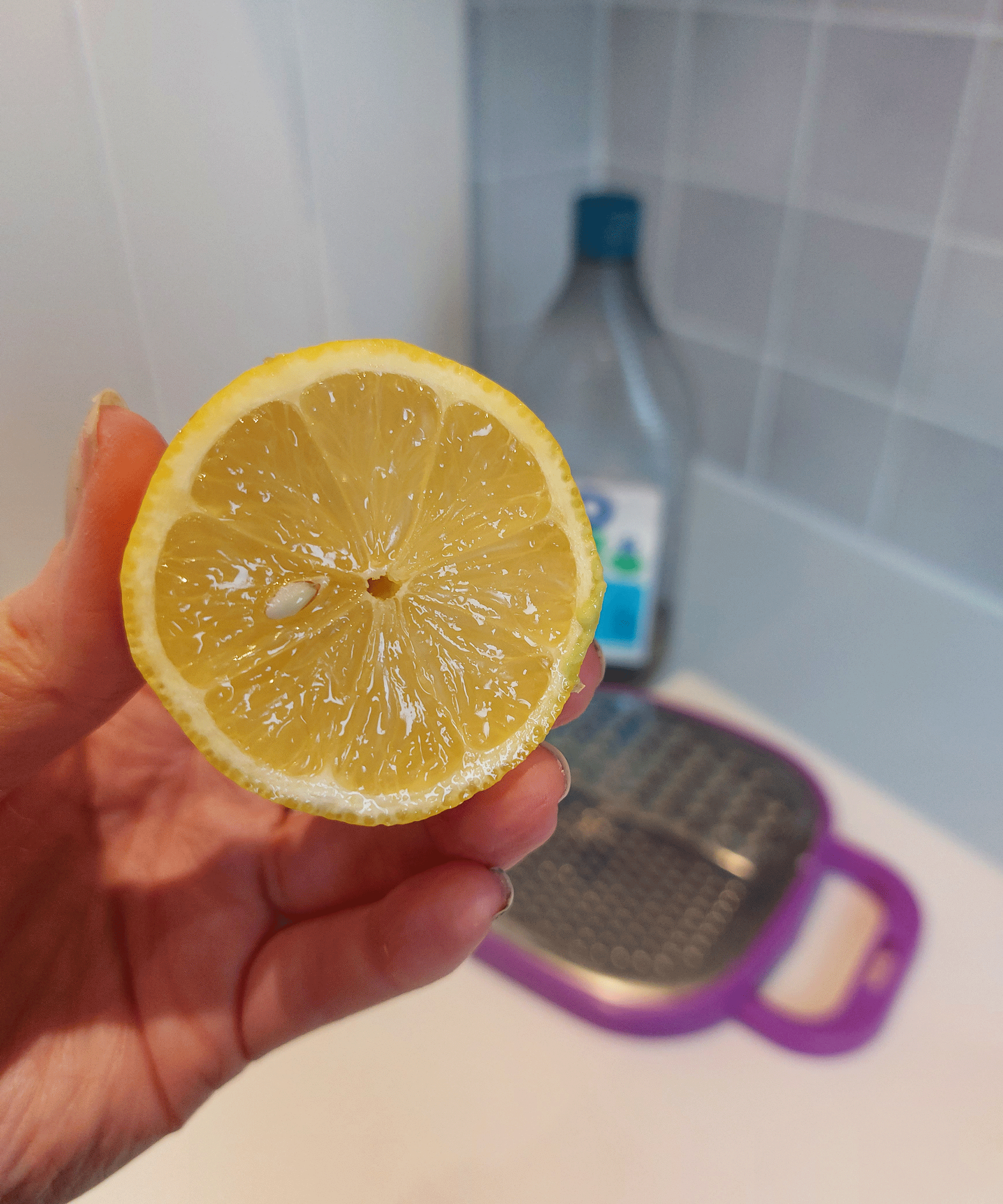 A woman holding a lemon which has been sliced in half horizontally with grater and detergent in background