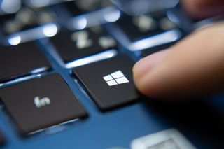 The Windows key being pushed on a blue laptop