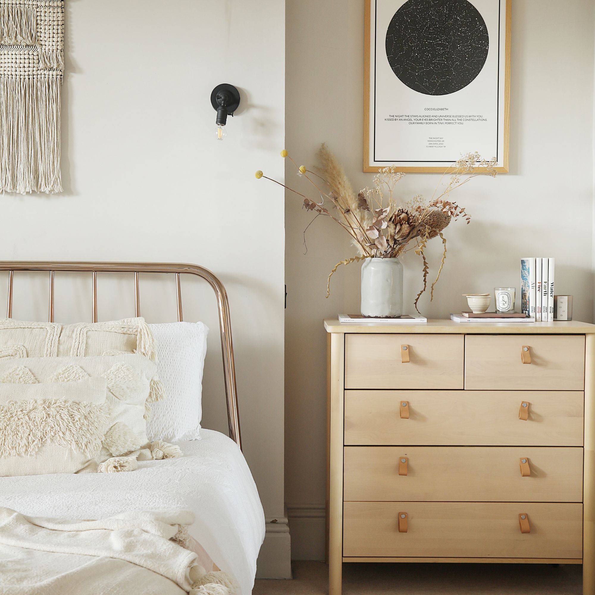 Neutral painted bedroom with neutral layered bed linen next to a wooden chest of drawers