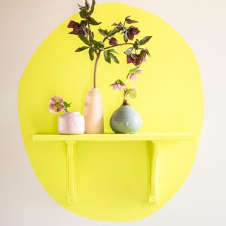 Yellow table against a circle yellow colored painted wall with flowers in vases