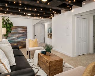 Basement with living area with sofa and chair, rug, trunk coffee table, white walls and dark beams