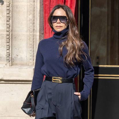 a woman with dark hair wearing a navy blue t shirt, gray trousers, and black sunglasses 