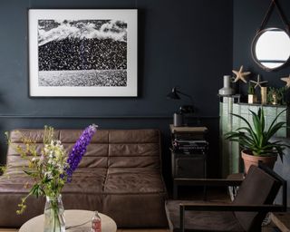 A dark living room with navy paint and slubby brown leather sofas
