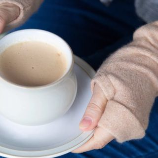 woman holding a cup of coffee wearing camel coloured fingerless gloves