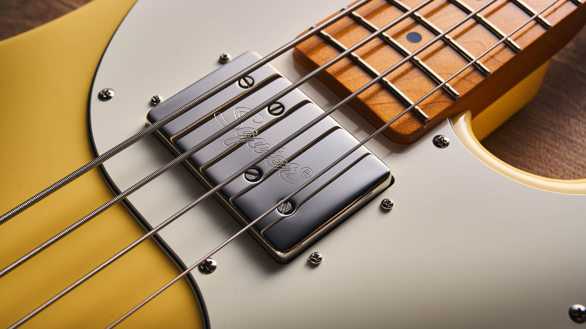 The Squier Classic Vibe Telecaster Bass is a fine-looking four-string in a custard-colored Vintage White, and is here photographed in close-up, against a plain wooden background. It has a single Wide Range humbucker.